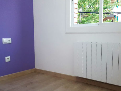 Detalle esquinero de suelo de parquet, con radiador, pared pintada de color y ventana
